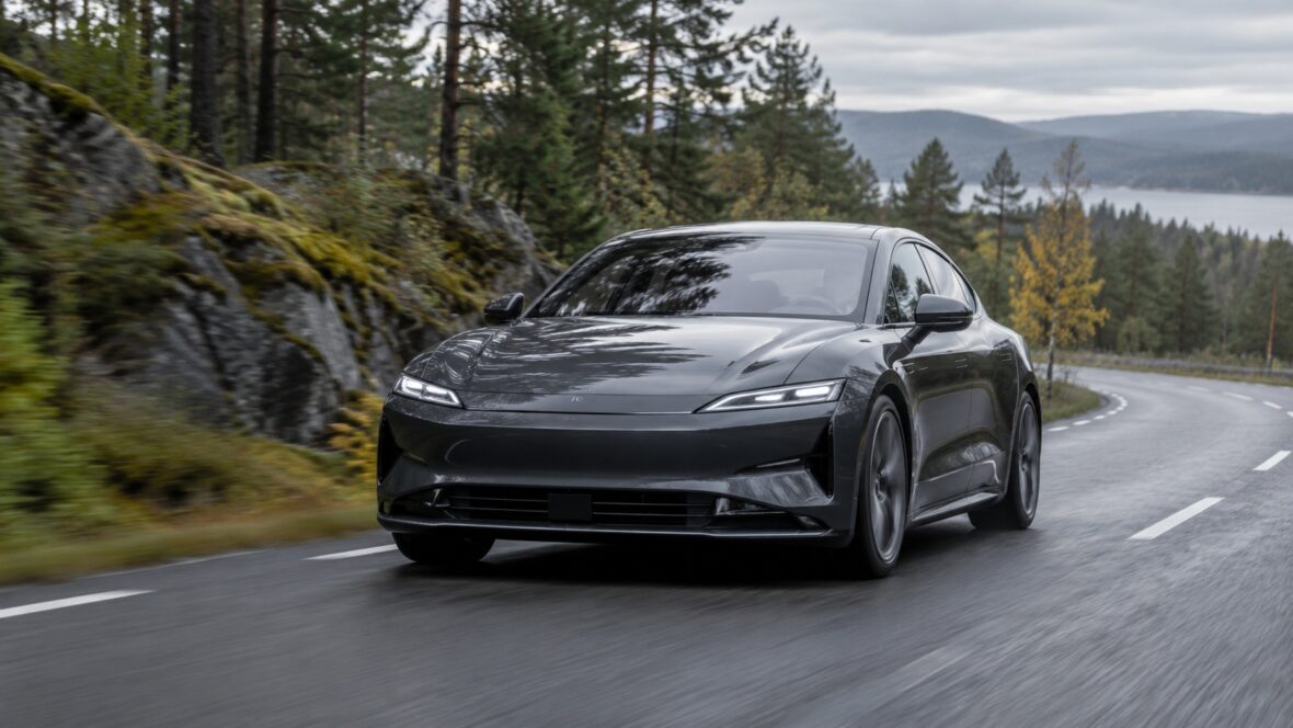Dark gray electric sport sedan on a curving forest mountain road.