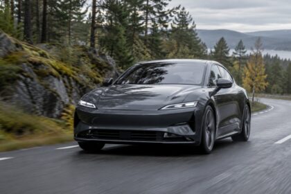 Dark gray electric sport sedan on a curving forest mountain road.